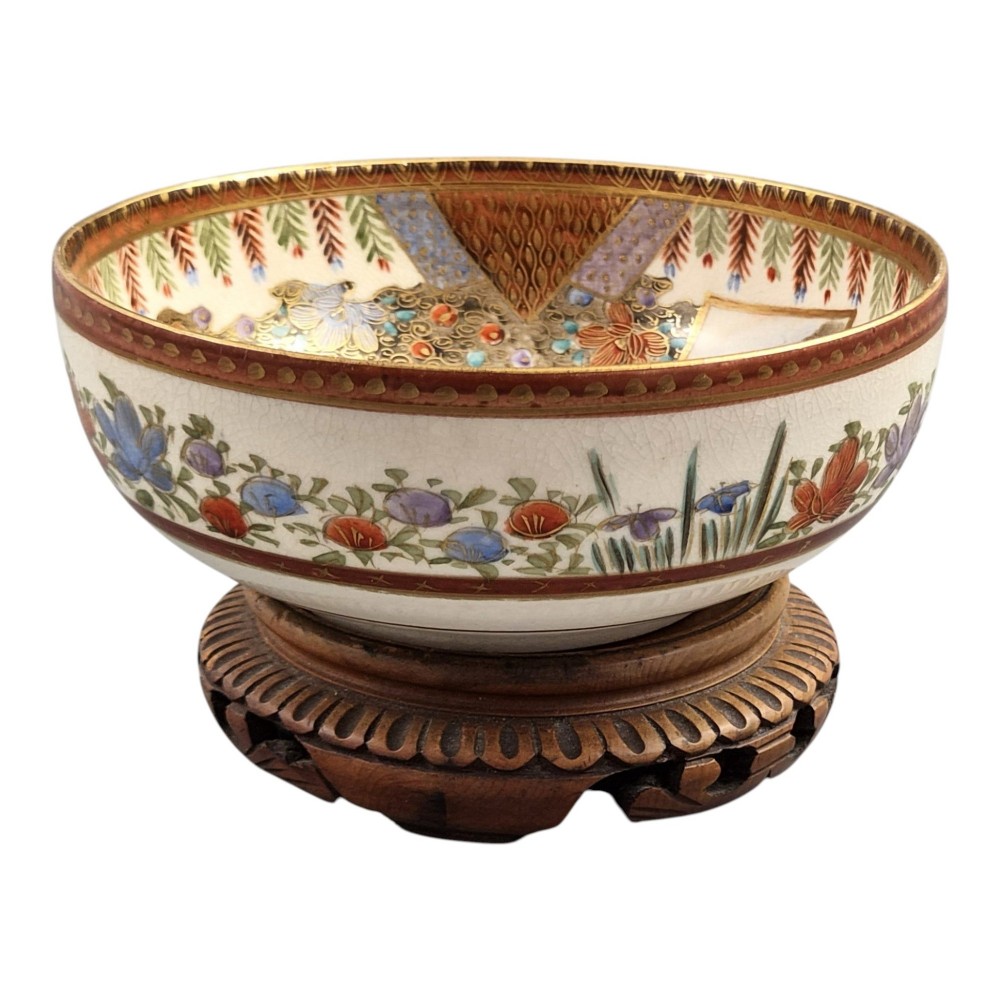 An antique Meiji period Japanese Satsuma earthenware bowl featuring hand-painted floral panels and gold detailing, elevated on a carved dark wooden base. View VI