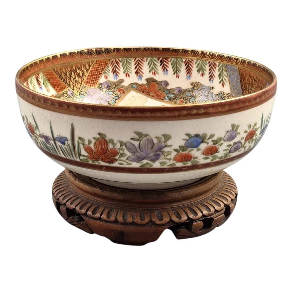 An antique Meiji period Japanese Satsuma earthenware bowl featuring hand-painted floral panels and gold detailing, elevated on a carved dark wooden base. View VII