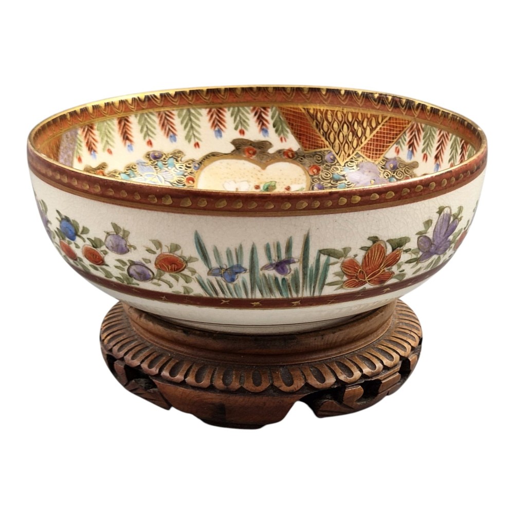 An antique Meiji period Japanese Satsuma earthenware bowl featuring hand-painted floral panels and gold detailing, elevated on a carved dark wooden base. View VIII