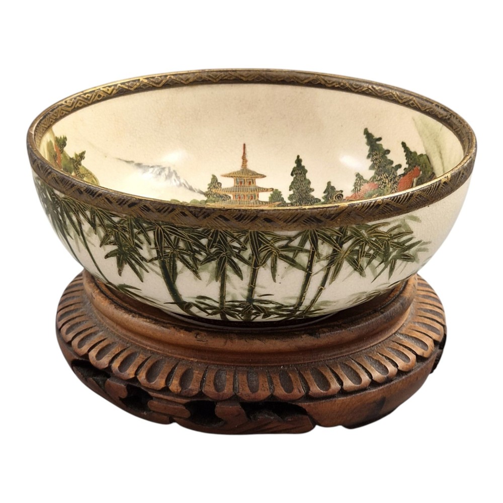 An antique cream earthenware bowl resting on a carved wooden base, decorated inside with hand-painted Japanese landscapes and figures, and finished with a bamboo pattern around the exterior. View VI