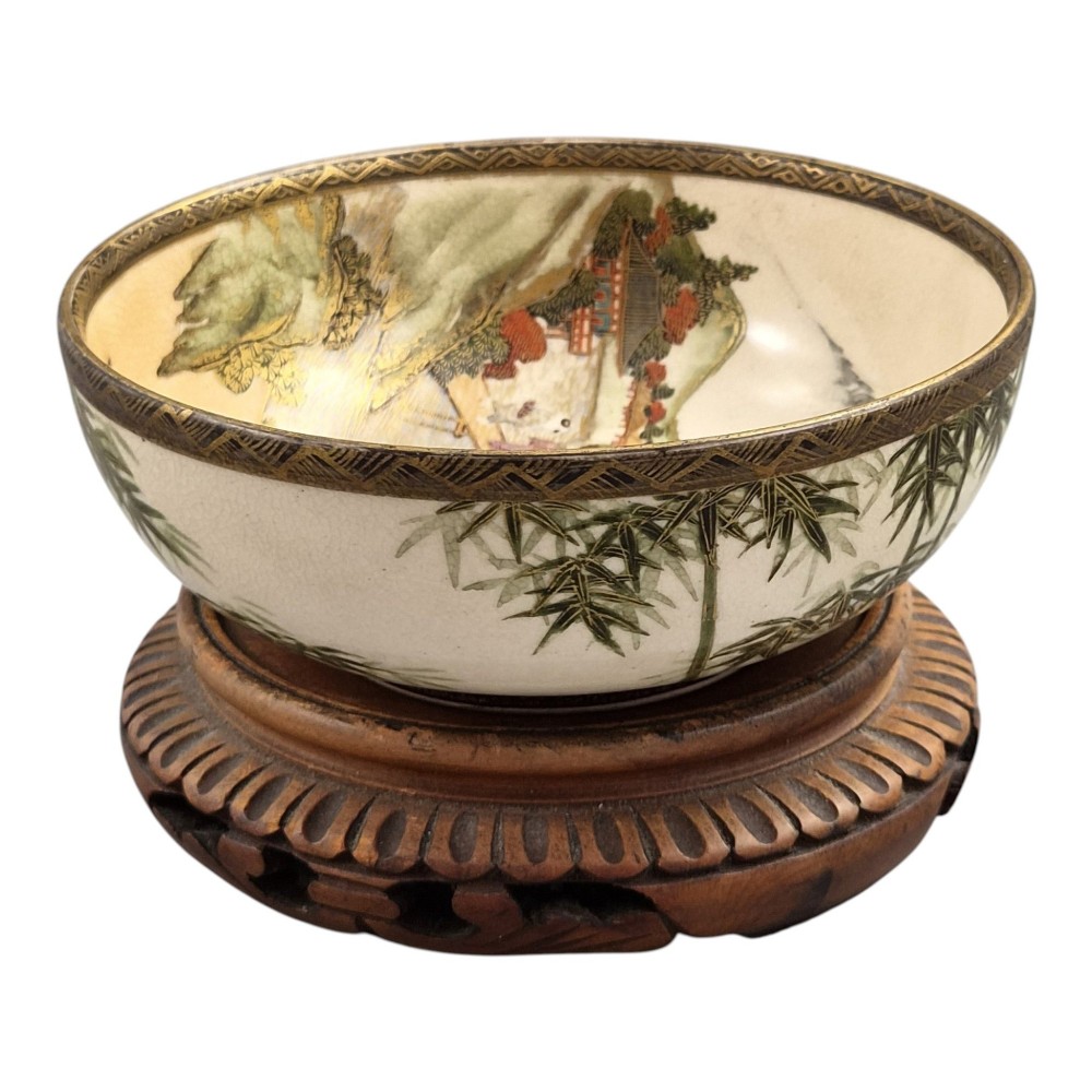 An antique cream earthenware bowl resting on a carved wooden base, decorated inside with hand-painted Japanese landscapes and figures, and finished with a bamboo pattern around the exterior. View VII