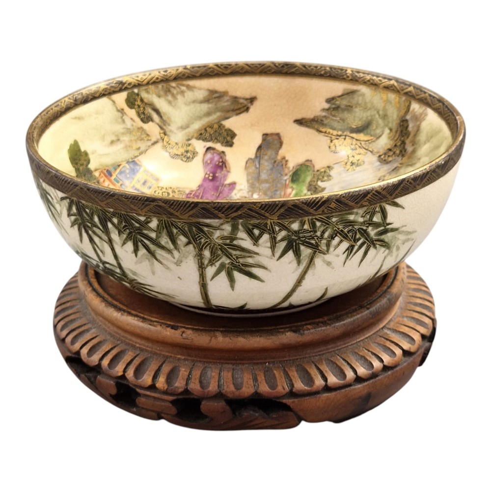 An antique cream earthenware bowl resting on a carved wooden base, decorated inside with hand-painted Japanese landscapes and figures, and finished with a bamboo pattern around the exterior. View VIII