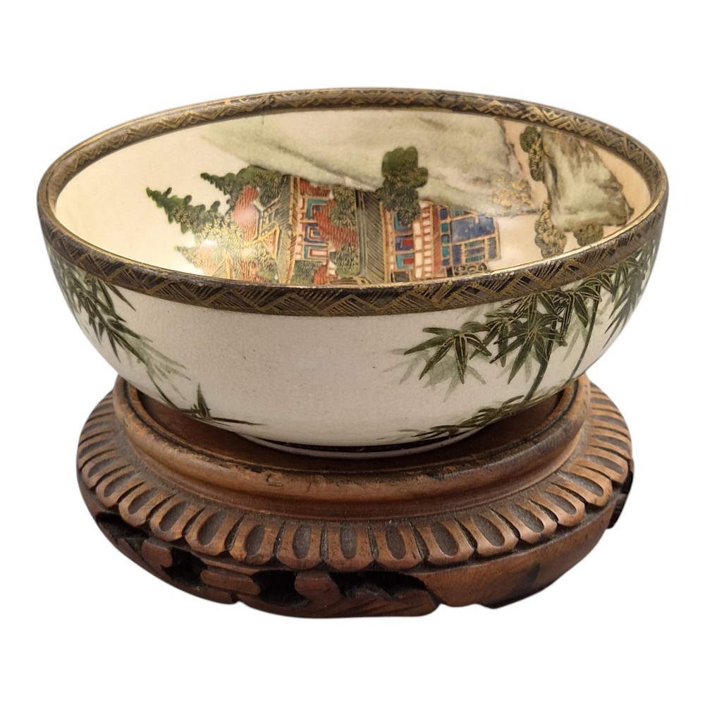An antique cream earthenware bowl resting on a carved wooden base, decorated inside with hand-painted Japanese landscapes and figures, and finished with a bamboo pattern around the exterior. View IX
