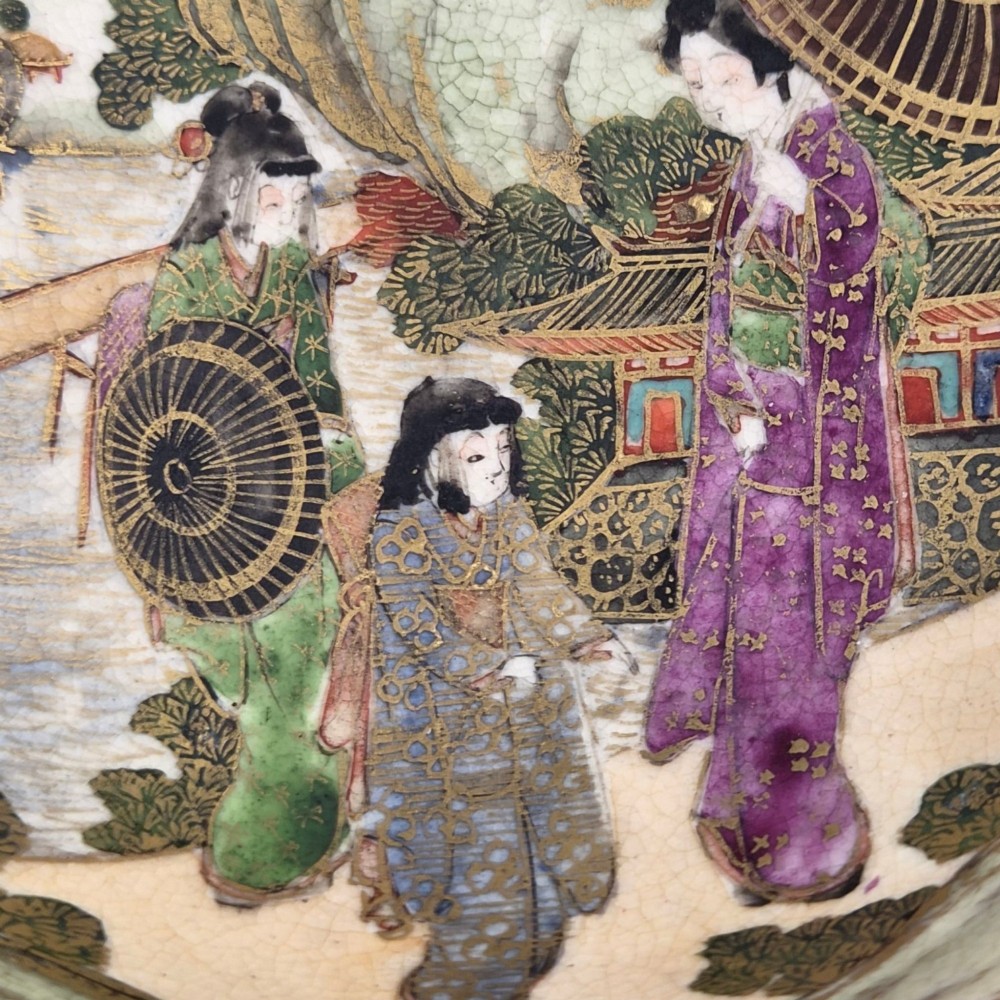 An antique cream earthenware bowl resting on a carved wooden base, decorated inside with hand-painted Japanese landscapes and figures, and finished with a bamboo pattern around the exterior. View XII