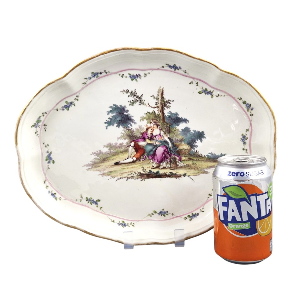 An oval 18th-century French porcelain tray featuring a hand-painted pastoral scene bordered by pink ribbon decoration and a scalloped gilt edge. View II