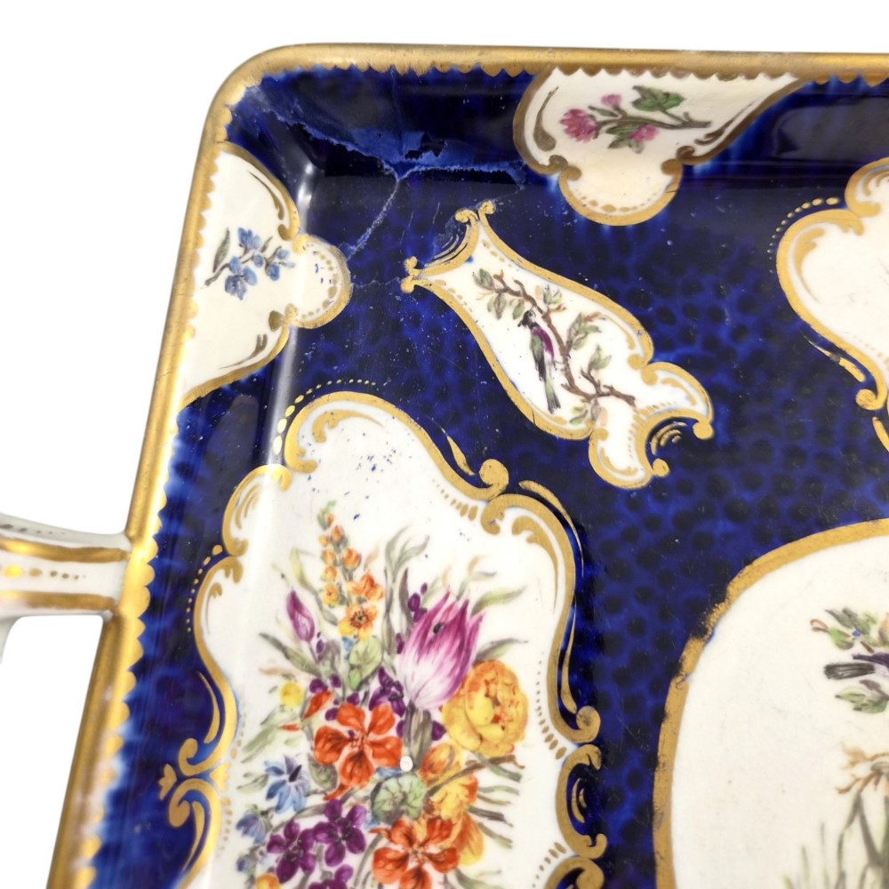 A rectangular mid-19th-century English porcelain tray featuring a dark cobalt blue ground, hand-painted exotic birds in a central oval vignette, floral reserves, and gilt handles. View XI