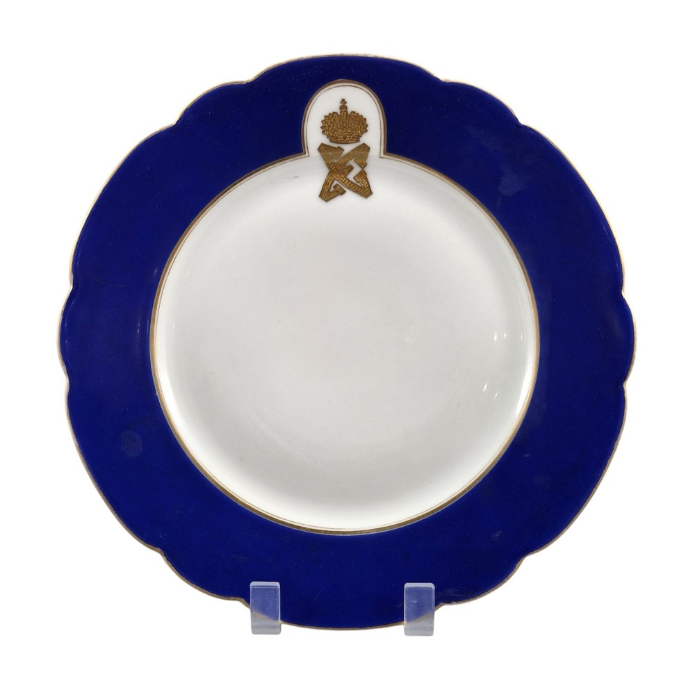 A white round porcelain plate featuring a thick cobalt blue scalloped border and a gilded Imperial monogram topped with a crown. View II