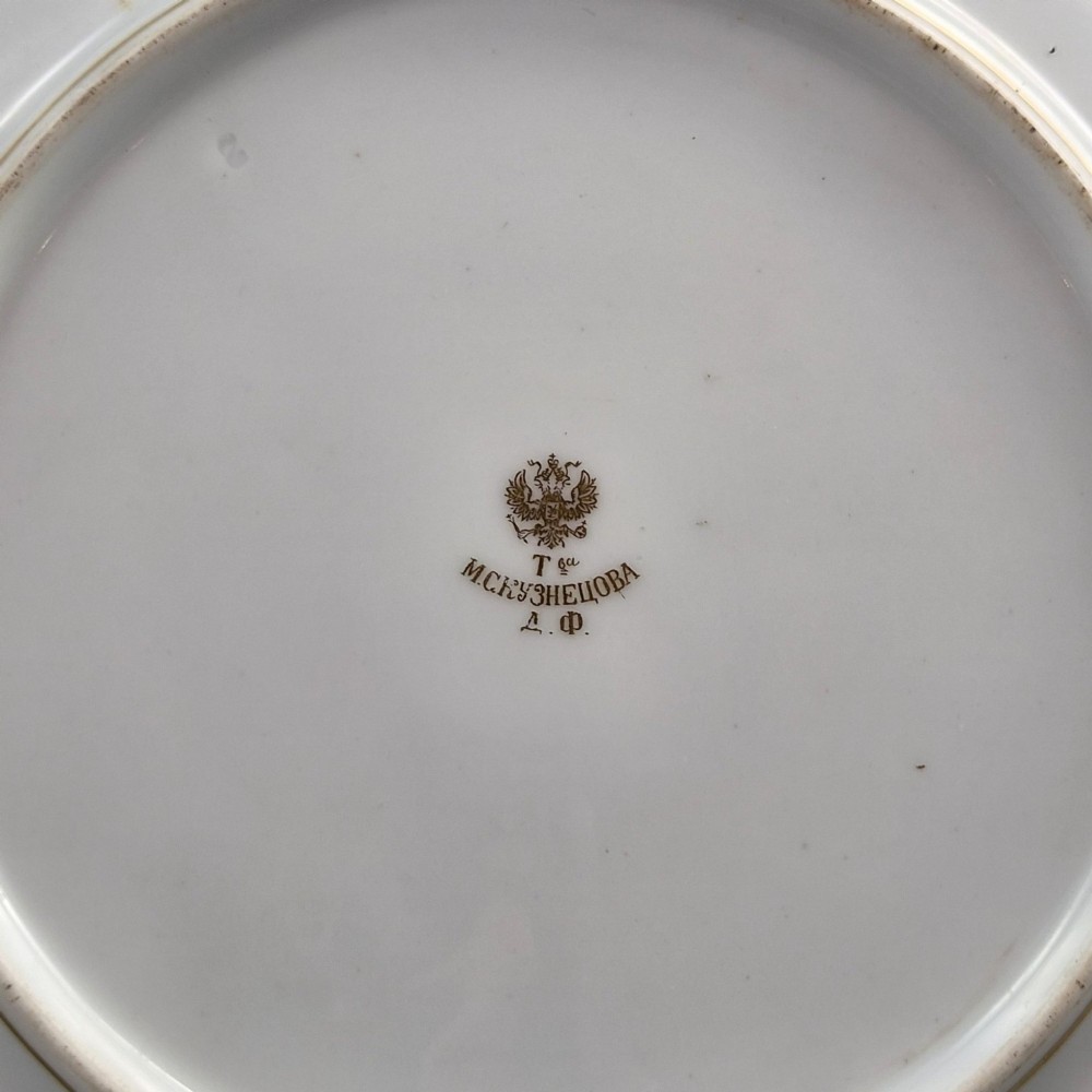 A white round porcelain plate featuring a thick cobalt blue scalloped border and a gilded Imperial monogram topped with a crown. View VI