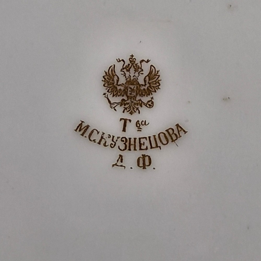 A white round porcelain plate featuring a thick cobalt blue scalloped border and a gilded Imperial monogram topped with a crown. View VII