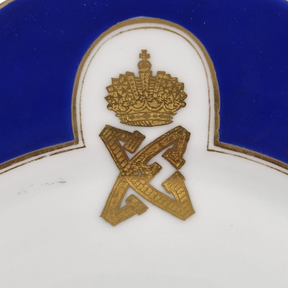 A white round porcelain plate featuring a thick cobalt blue scalloped border and a gilded Imperial monogram topped with a crown. View IX