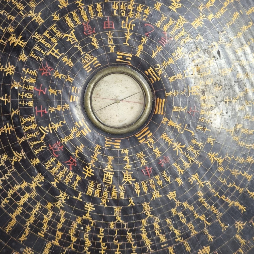 A circular antique Chinese Luopan geomantic compass crafted from dark lacquered wood featuring multiple concentric rings of gilded Chinese characters and a central brass magnetic dial. View III