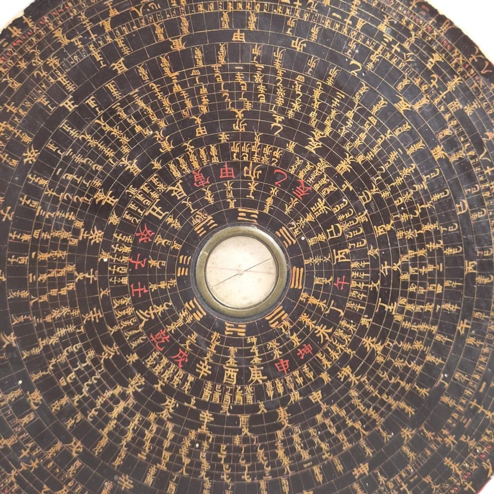 A circular antique Chinese Luopan geomantic compass crafted from dark lacquered wood featuring multiple concentric rings of gilded Chinese characters and a central brass magnetic dial. View IV