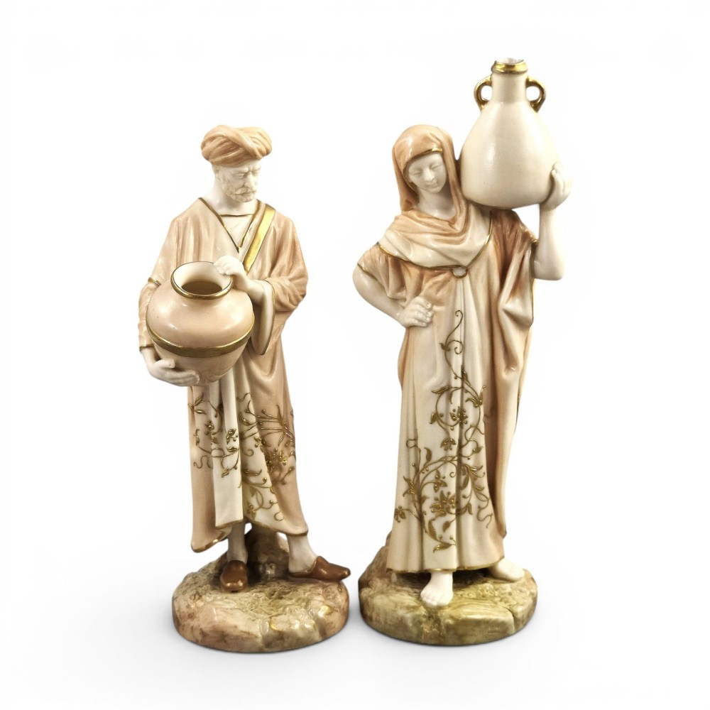 A pair of Royal Worcester blush ivory porcelain figures depicting a male and female Cairo water carrier with gilded accents.