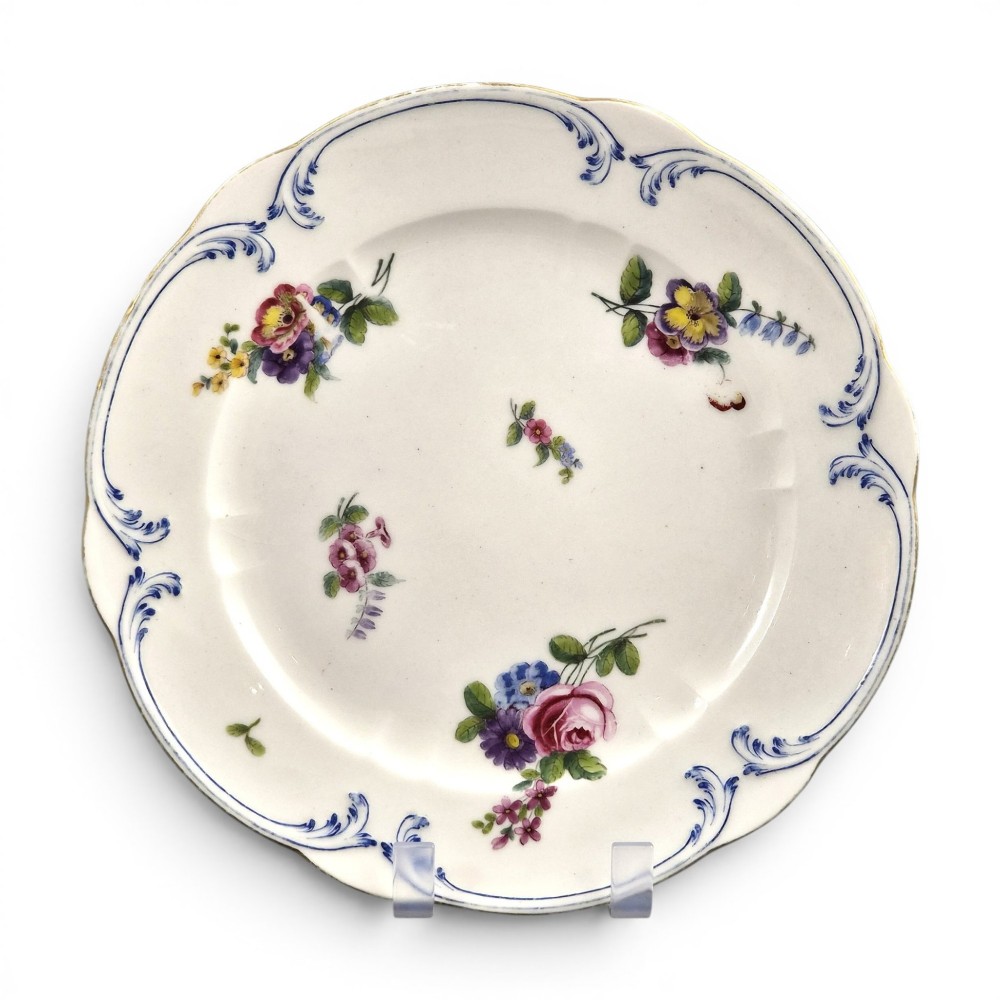 An 18th-century circular white soft-paste porcelain plate decorated with hand-painted floral sprays and a scalloped rim with blue feathered scroll details.