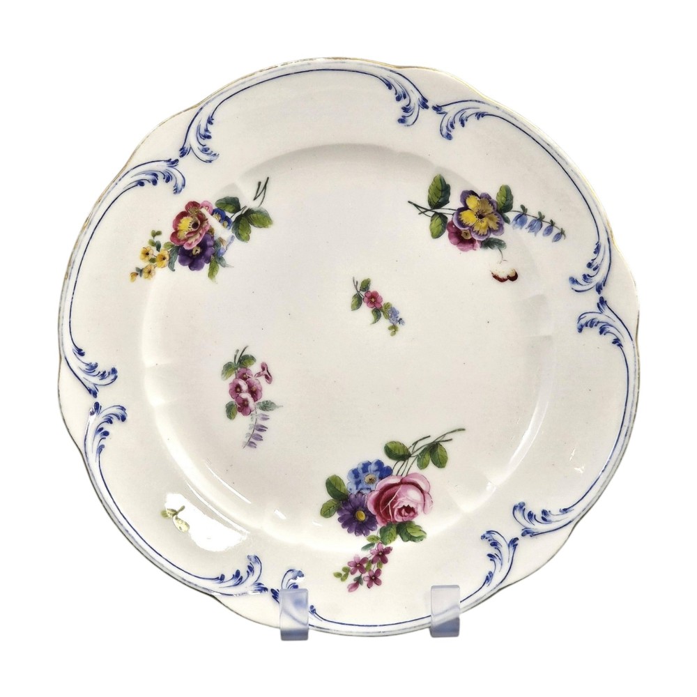 An 18th-century circular white soft-paste porcelain plate decorated with hand-painted floral sprays and a scalloped rim with blue feathered scroll details. View II