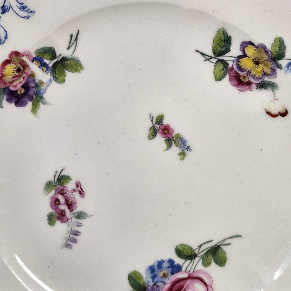 An 18th-century circular white soft-paste porcelain plate decorated with hand-painted floral sprays and a scalloped rim with blue feathered scroll details. View IV