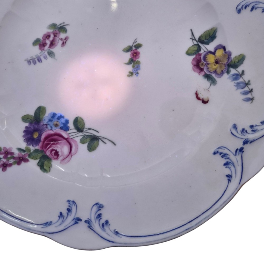 An 18th-century circular white soft-paste porcelain plate decorated with hand-painted floral sprays and a scalloped rim with blue feathered scroll details. View VIII