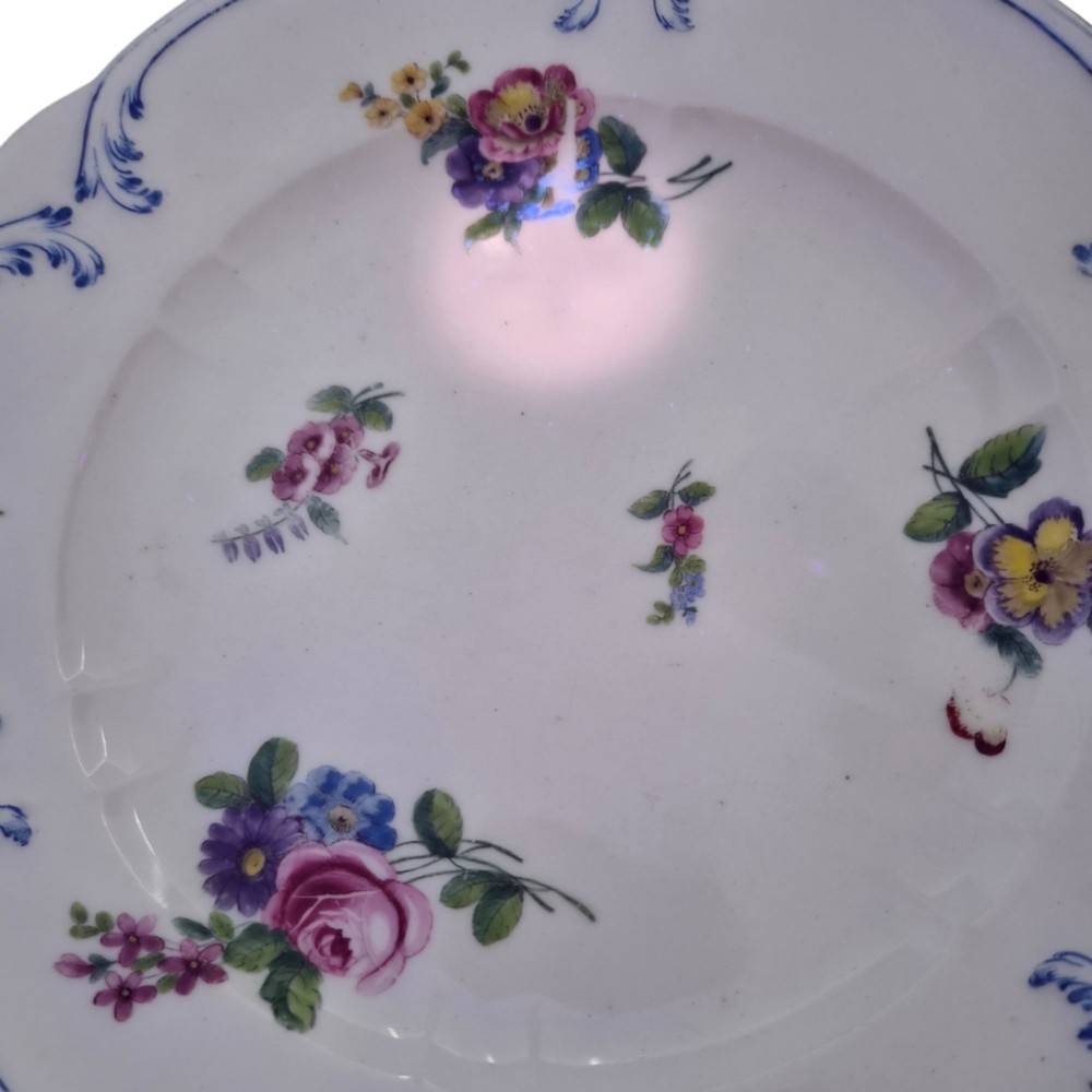 An 18th-century circular white soft-paste porcelain plate decorated with hand-painted floral sprays and a scalloped rim with blue feathered scroll details. View IX