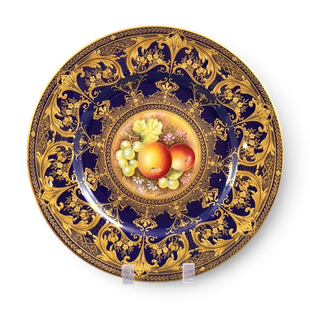 A circular Royal Worcester porcelain cabinet plate featuring a hand-painted fruit still life surrounded by a deep cobalt blue border decorated with intricate gold gilding.