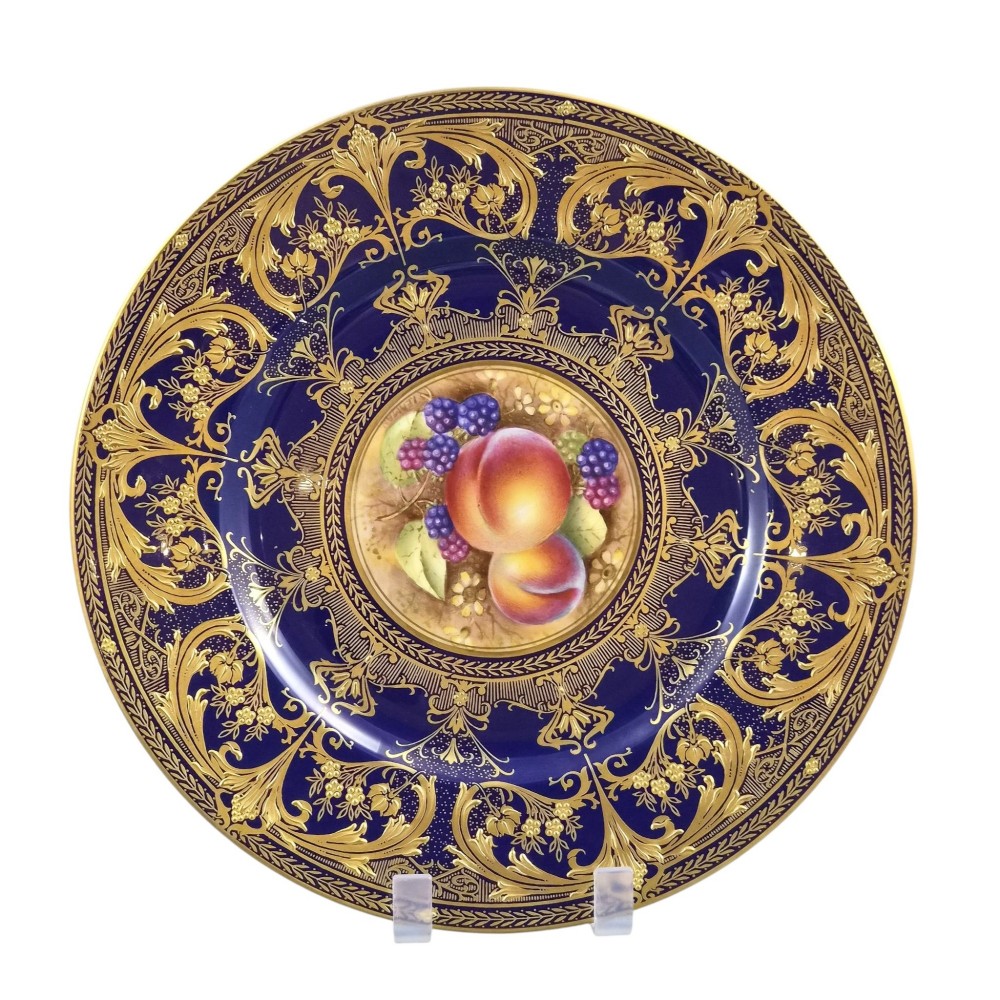 A circular porcelain cabinet plate featuring a central hand-painted still life of peaches and blackberries, surrounded by a broad cobalt blue border adorned with intricate gold gilding. View V