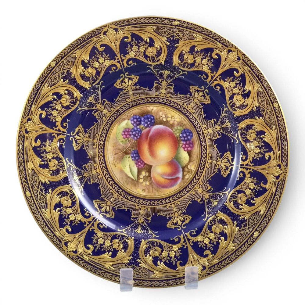 A circular porcelain cabinet plate featuring a central hand-painted still life of peaches and blackberries, surrounded by a broad cobalt blue border adorned with intricate gold gilding.