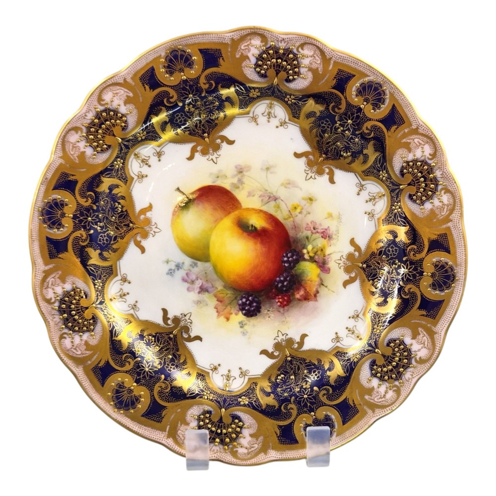 A circular porcelain cabinet plate featuring a central hand-painted fruit study surrounded by an ornate cobalt blue and heavily gilded scalloped rim. View X