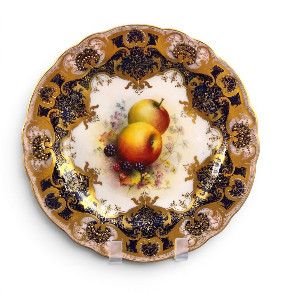 A circular Royal Worcester porcelain cabinet plate featuring hand-painted apples and berries in the centre surrounded by a cobalt blue border with heavy gold gilding.