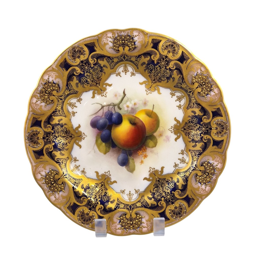 A circular porcelain cabinet plate featuring a central hand-painted motif of apples and grapes surrounded by an ornate cobalt blue and heavily gilded rococo border.