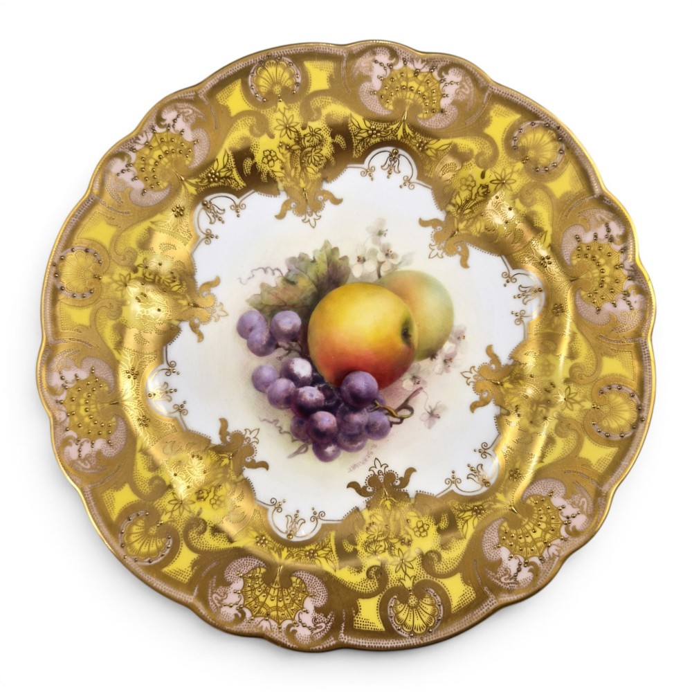 A circular Royal Worcester ceramic cabinet plate featuring a central hand-painted motif of apples and grapes surrounded by a gold gilt and yellow scrollwork border.