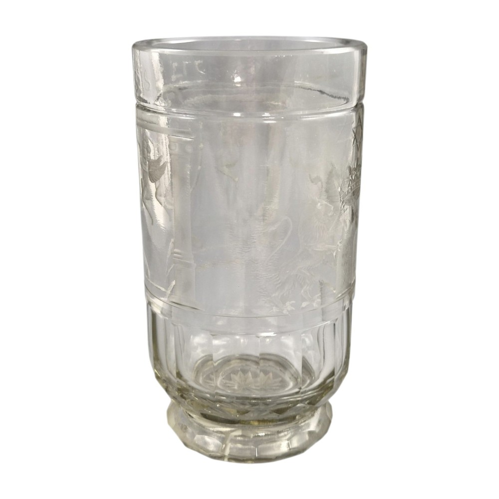 A large clear glass beaker featuring detailed wheel-engraved ceremonial iconography, vertical fluted panels near the lower rim, and a faceted base.