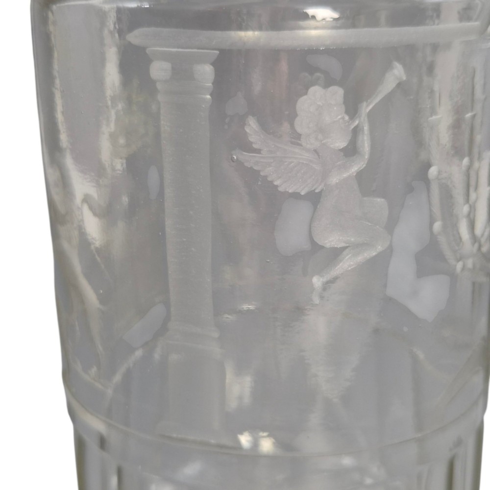 A large clear glass beaker featuring detailed wheel-engraved ceremonial iconography, vertical fluted panels near the lower rim, and a faceted base. View V