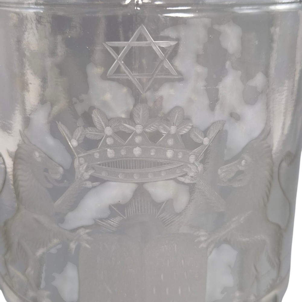 A large clear glass beaker featuring detailed wheel-engraved ceremonial iconography, vertical fluted panels near the lower rim, and a faceted base. View X