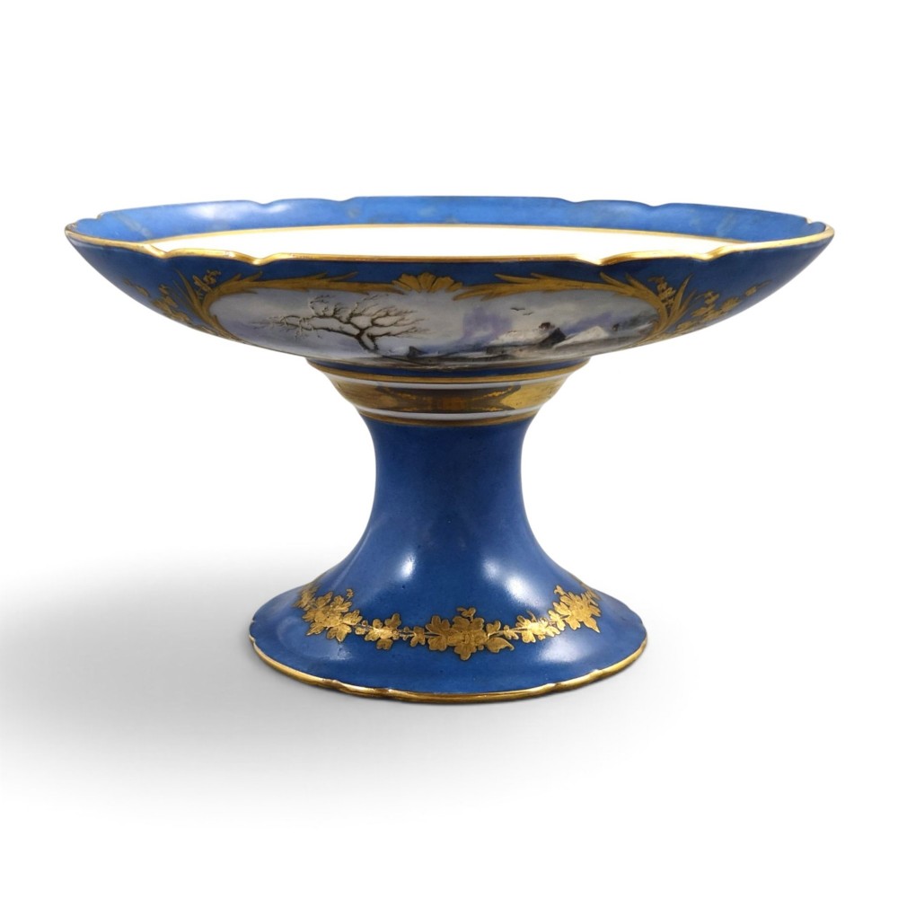 A cobalt blue and gilt porcelain tazza elevated on a pedestal base, adorned with a hand-painted winter landscape cartouche.