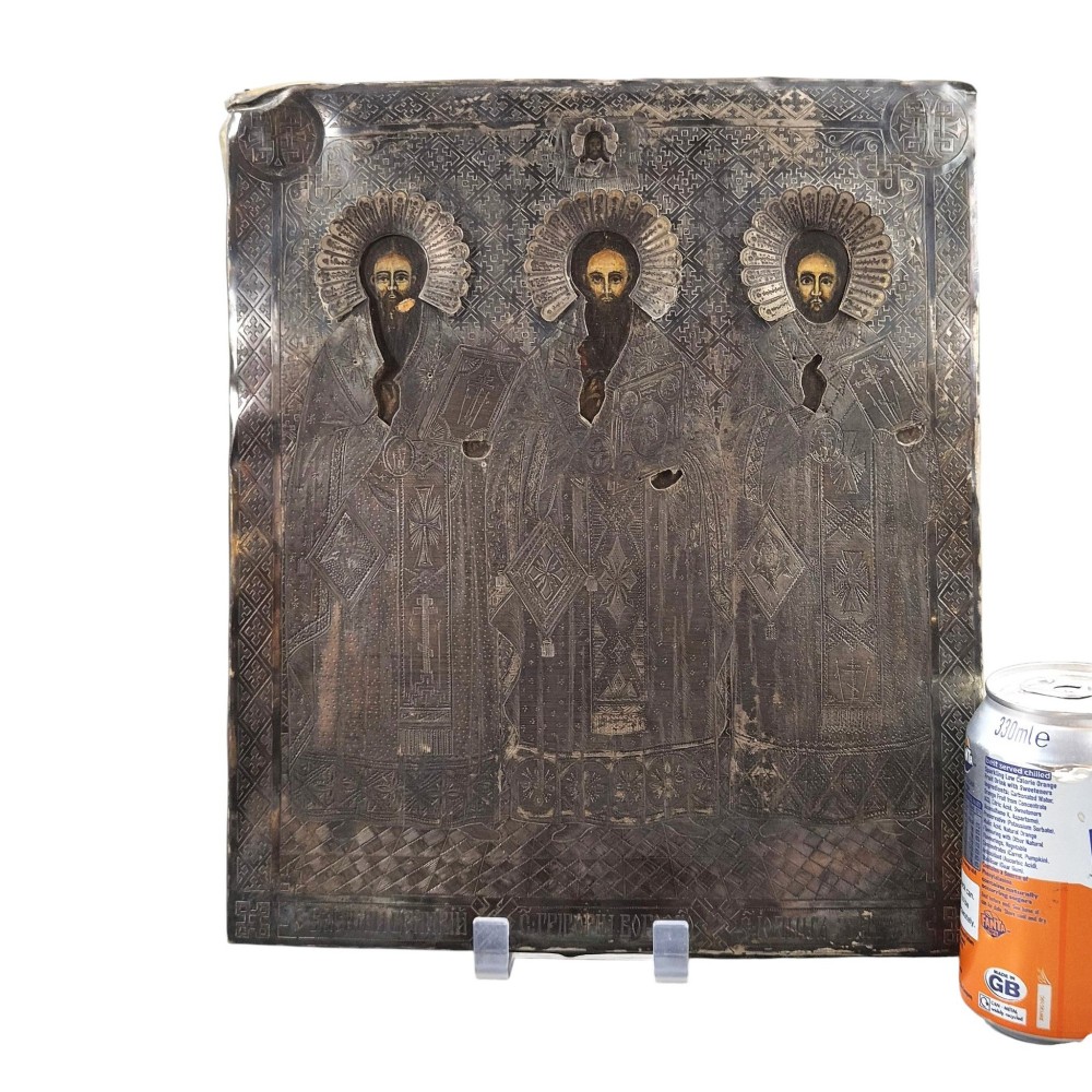 A rectangular antique Orthodox silver icon featuring repousse depictions of the Three Holy Hierarchs with detailed halos and Cyrillic script along the bottom edge. View III