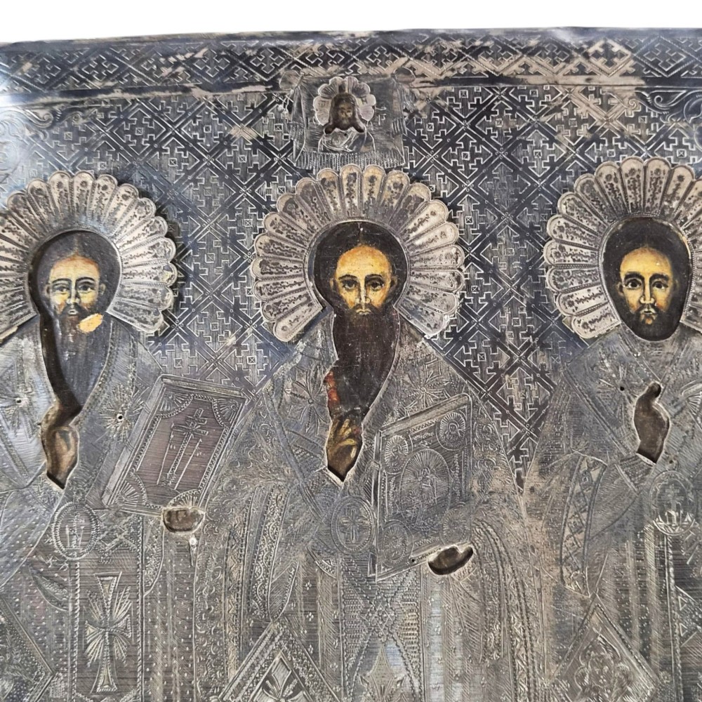 A rectangular antique Orthodox silver icon featuring repousse depictions of the Three Holy Hierarchs with detailed halos and Cyrillic script along the bottom edge. View IV