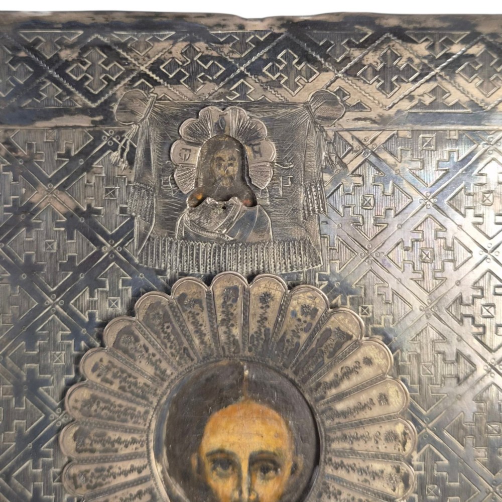 A rectangular antique Orthodox silver icon featuring repousse depictions of the Three Holy Hierarchs with detailed halos and Cyrillic script along the bottom edge. View V