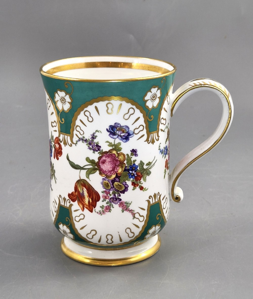 An antique French porcelain cabinet mug featuring a green ground with hand-painted floral bouquets and gilt scroll detailing.