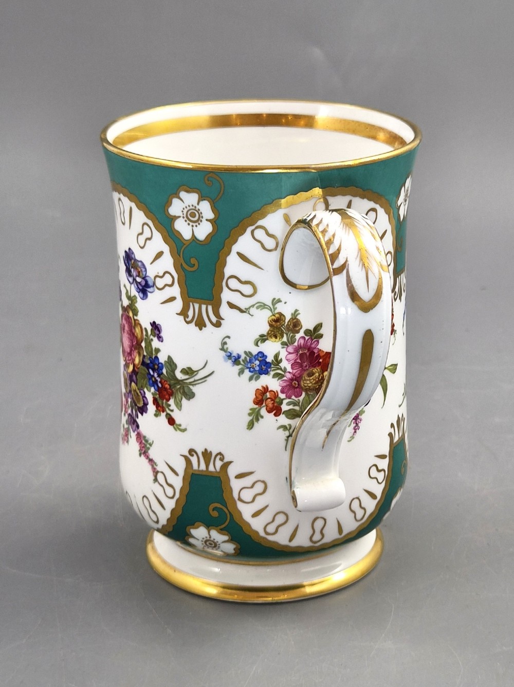 An antique French porcelain cabinet mug featuring a green ground with hand-painted floral bouquets and gilt scroll detailing. View II
