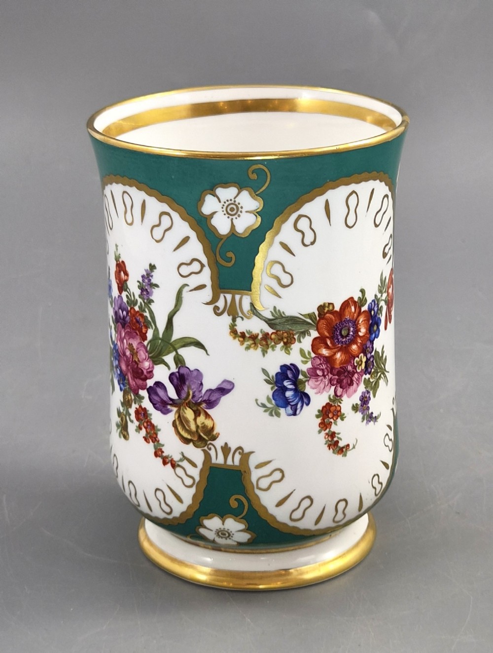 An antique French porcelain cabinet mug featuring a green ground with hand-painted floral bouquets and gilt scroll detailing. View V