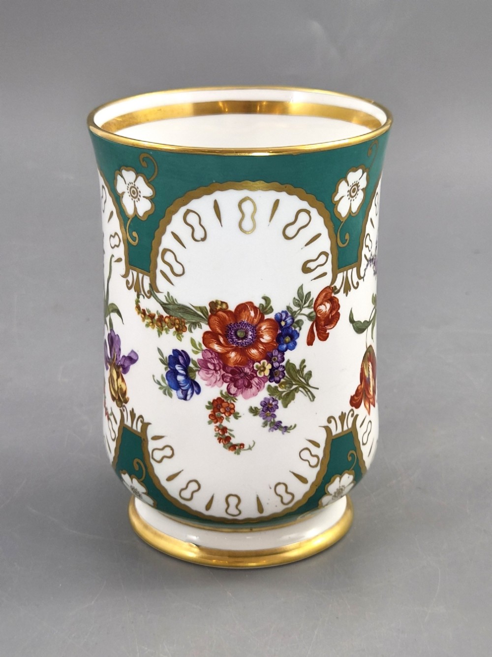 An antique French porcelain cabinet mug featuring a green ground with hand-painted floral bouquets and gilt scroll detailing. View VI