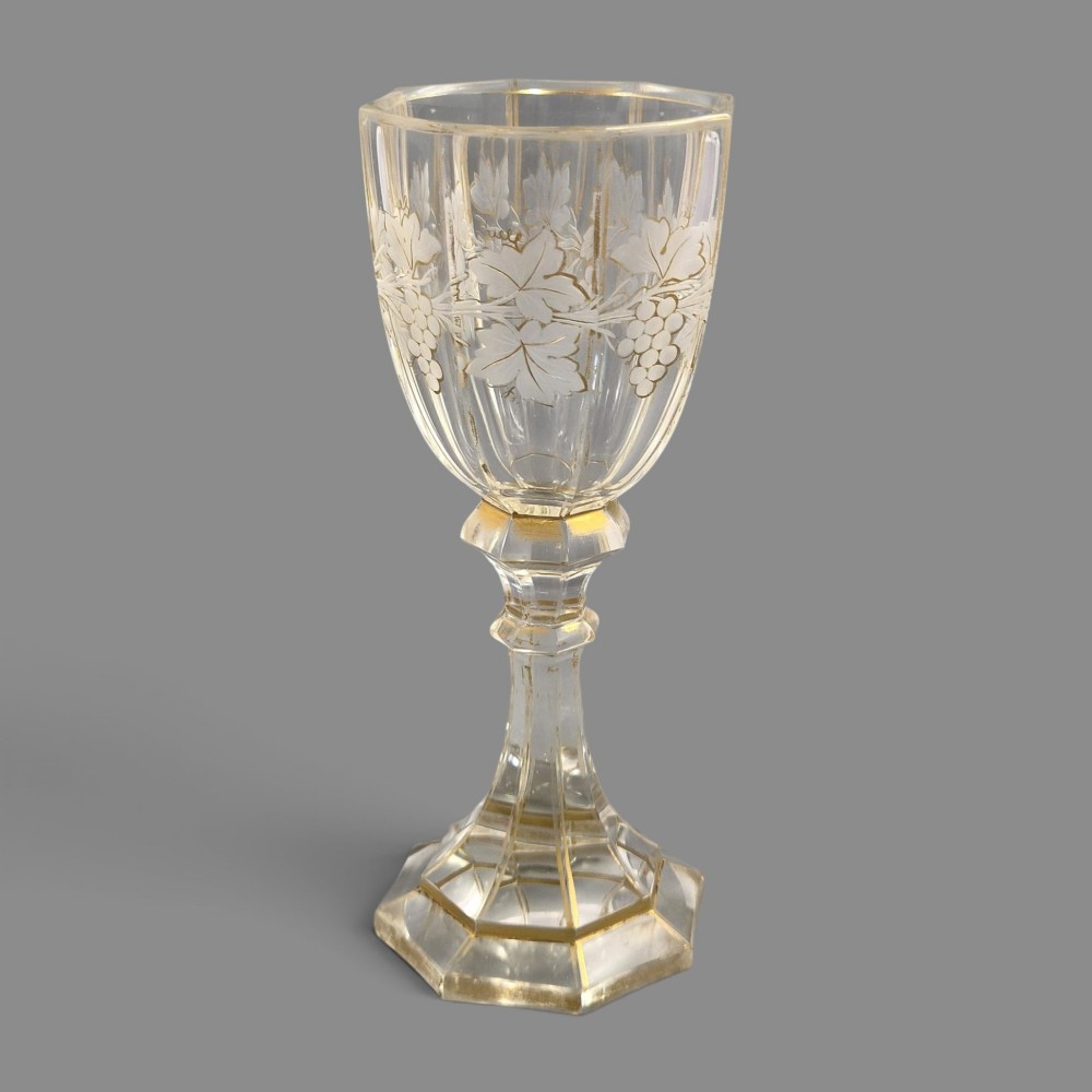 A clear Bohemian crystal romer goblet featuring wheel-engraved grapevine motifs, a faceted stem, and gilt highlight accents on a hexagonal foot. View II