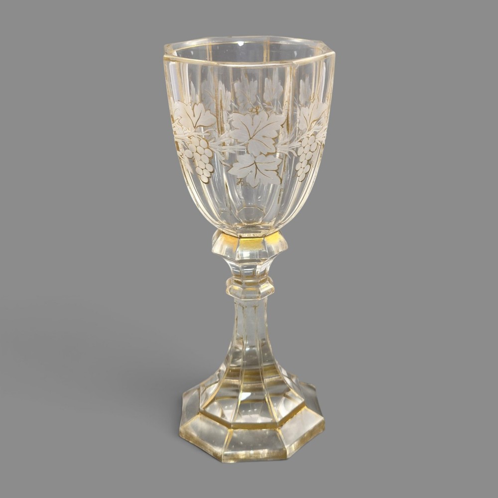 A clear Bohemian crystal romer goblet featuring wheel-engraved grapevine motifs, a faceted stem, and gilt highlight accents on a hexagonal foot. View VIII