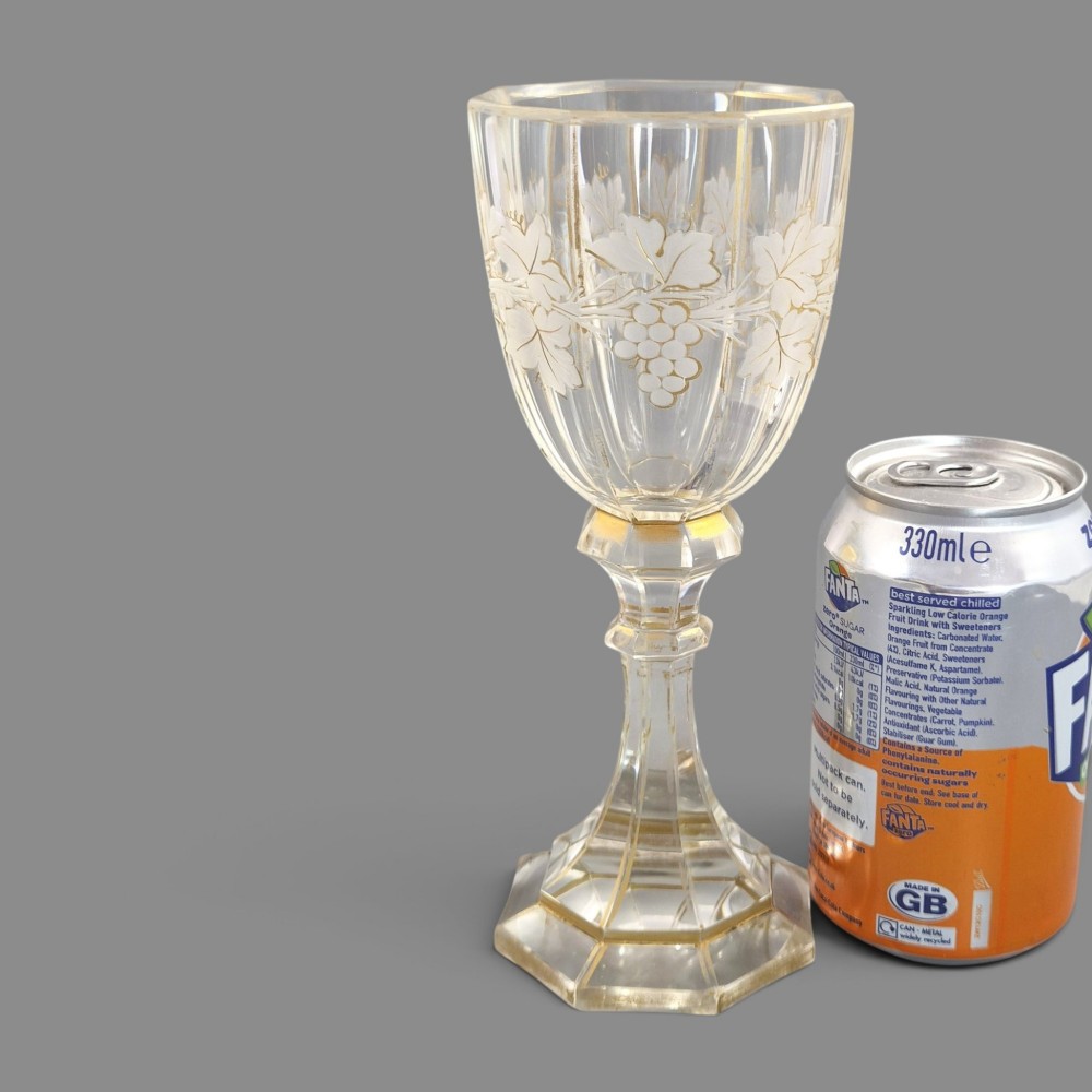 A clear Bohemian crystal romer goblet featuring wheel-engraved grapevine motifs, a faceted stem, and gilt highlight accents on a hexagonal foot. View XII