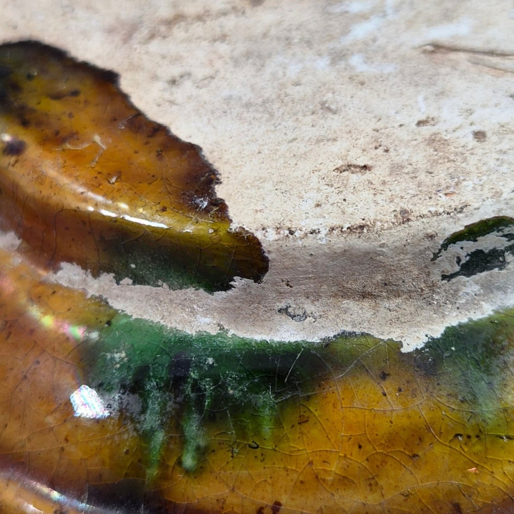 A squat antique Chinese ceramic water vessel featuring a green glazed upper shoulder, a square rim, and an amber-glazed moulded floral band around the middle. View X