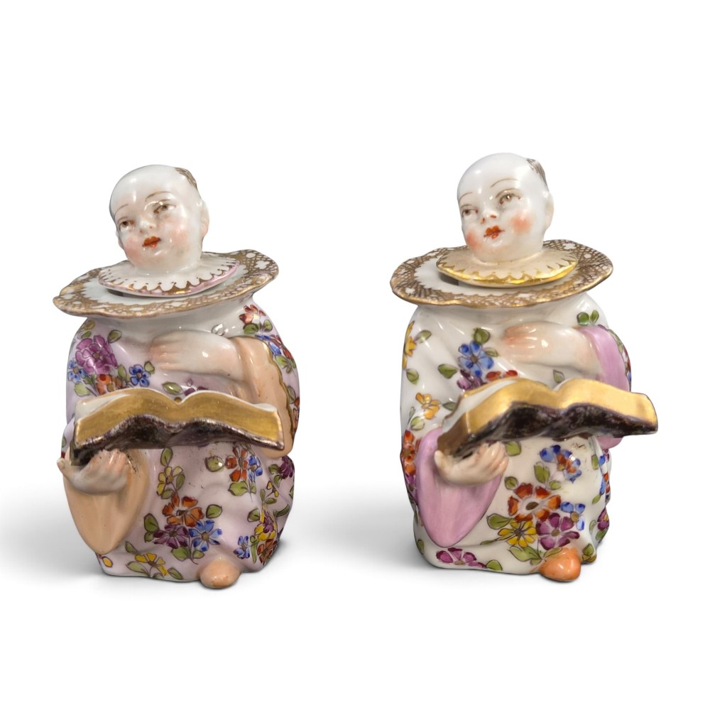 A pair of antique French Samson porcelain figural inkwells depicting singing boys wearing floral robes and gilt-rimmed ruffs while holding open songbooks.