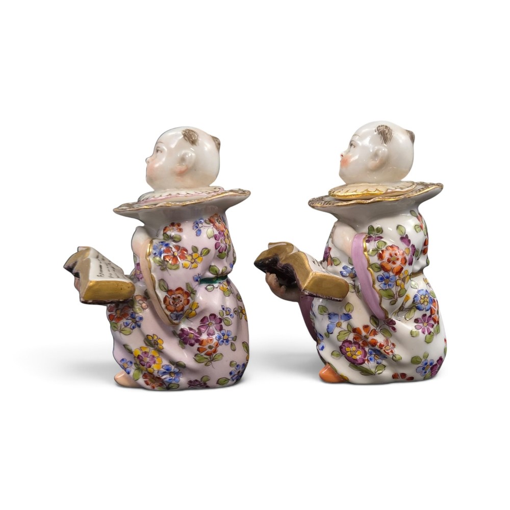 A pair of antique French Samson porcelain figural inkwells depicting singing boys wearing floral robes and gilt-rimmed ruffs while holding open songbooks. View II