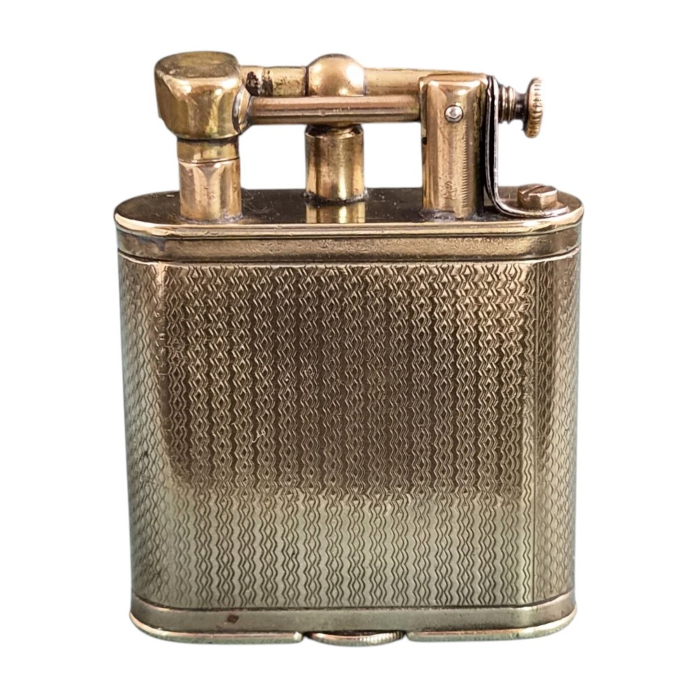 A 1920s Dunhill Unique gold-plated petrol lighter featuring an engine-turned pattern and a straight-arm lift mechanism.
