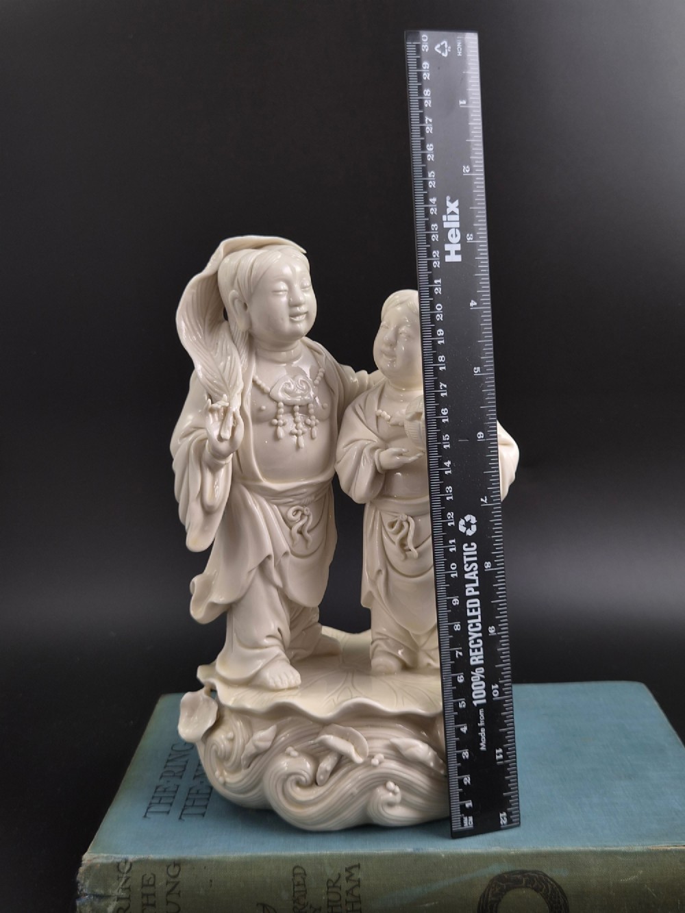 A cream white glazed porcelain figure group featuring two standing figures positioned on a lotus leaf and wave carved base. View XII