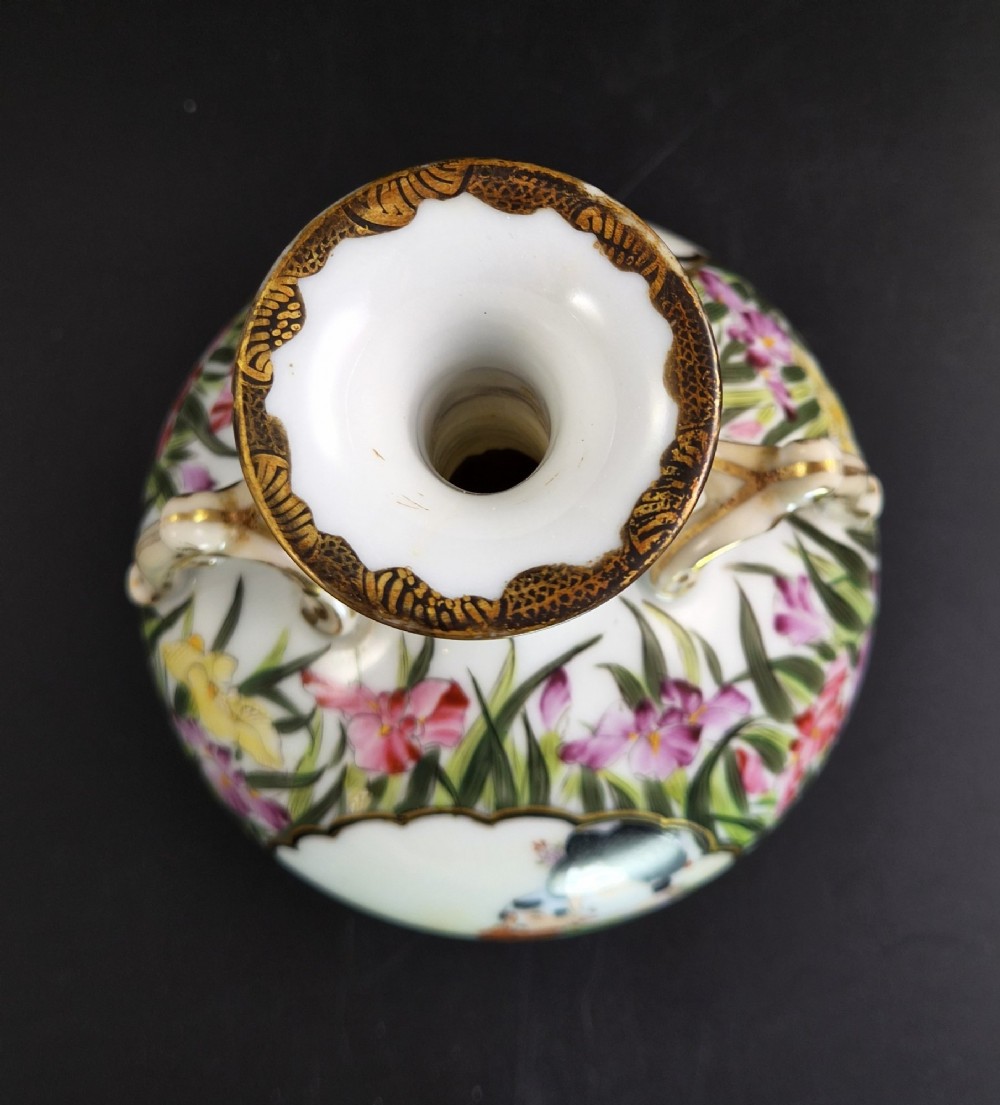A pair of Japanese Yokohama porcelain vases decorated with hand-painted figures, floral irises, twin gilt handles, and gilded neck details. View V