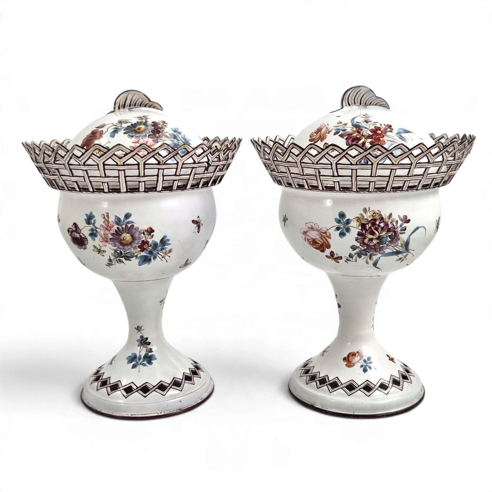 A pair of off-white 19th-century French tole peinte chestnut urns featuring hand-painted botanical motifs, pierced lattice galleries, and shell-form finials on the lids.